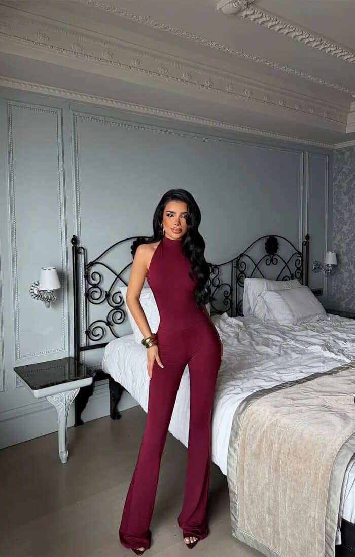Femme portant une combinaison halter bordeaux dans une chambre chic.