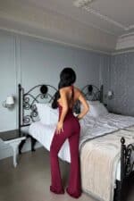 Femme en combinaison halter bordeaux dans une chambre chic.