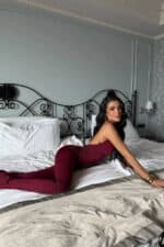 Femme en combinaison halter bordeaux sur un lit dans une chambre chic.