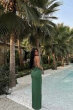 Femme portant une robe longue halter vert sauge dans un jardin tropical.