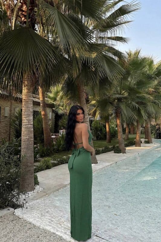 Femme portant une robe longue halter vert sauge dans un jardin tropical.