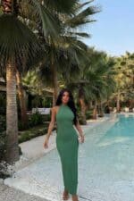 Femme portant une robe longue halter vert sauge près de la piscine.